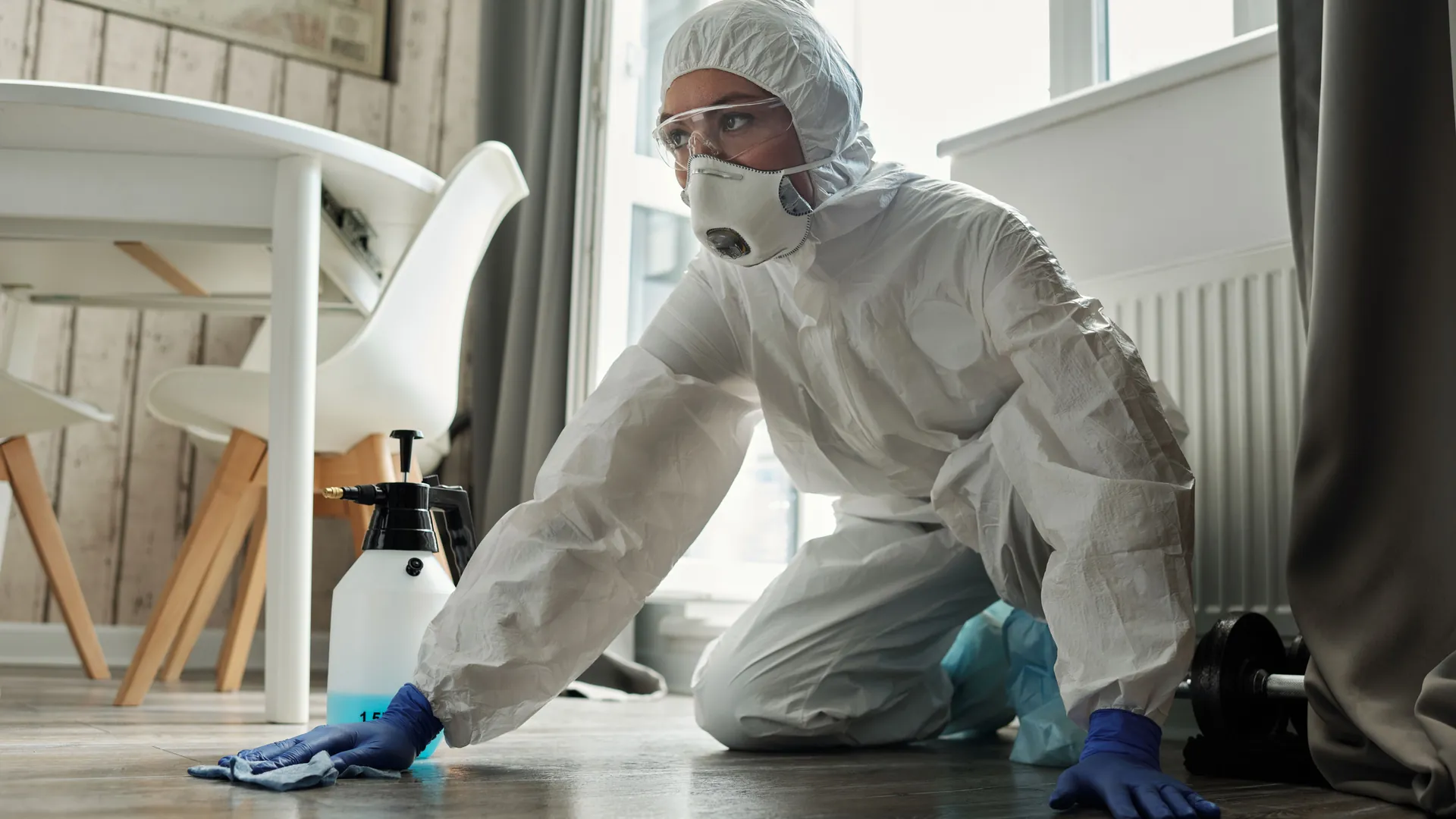 Worker in a full protective suit and mask wiping down a floor with disinfectant