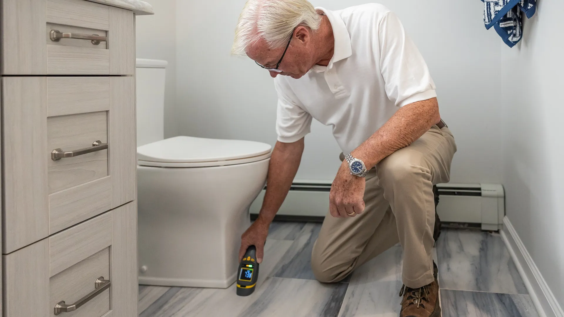Man kneeling beside a toilet with a handheld device to check the bathroom floor